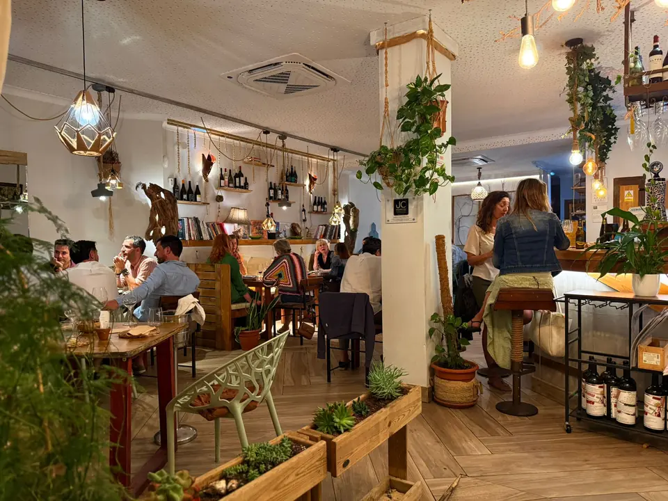 El salón de Raizes lleno, con lámparas colgantes, plantas y la bodega en las paredes